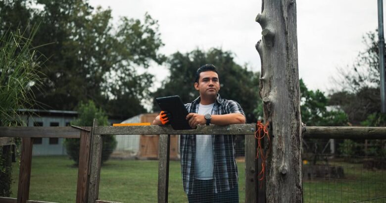 Man holding tablet standing by a wooden fence outdoors